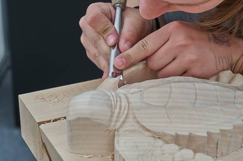 A woman hand-carving a wooden turtle.