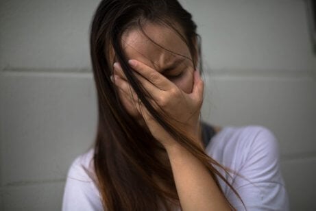 A woman with her hand on her face, feeling extremely distressed.