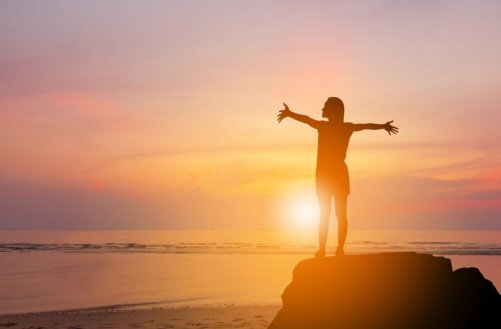 A woman with arms outstretched in front of the sun.