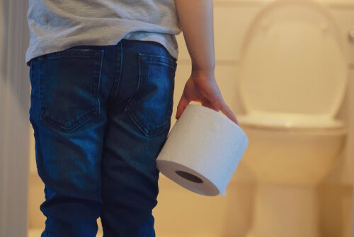 A child holding a roll of toilet paper by the toilet.
