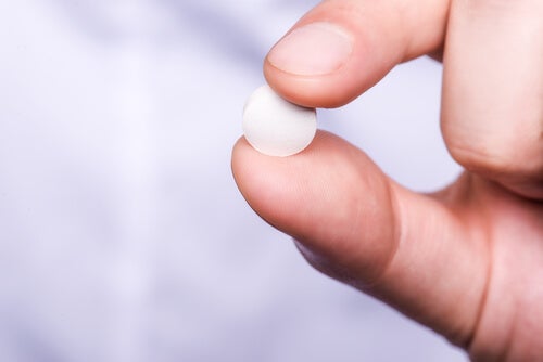 A person holding a pill between their fingers.