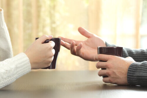 A close-up of two hands gesturing as people talk with coffee mugs in hand. 
