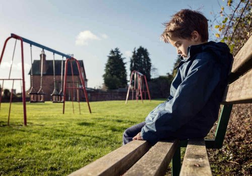 A kid sitting alone on a park bench.