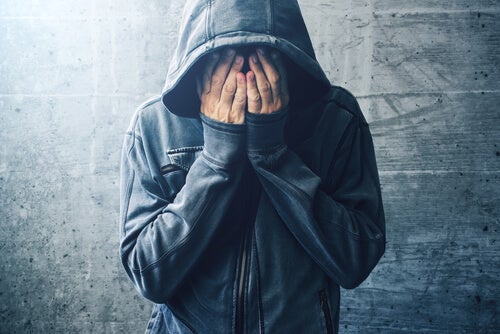 A person wearing a hoodie, crying into their hands. 