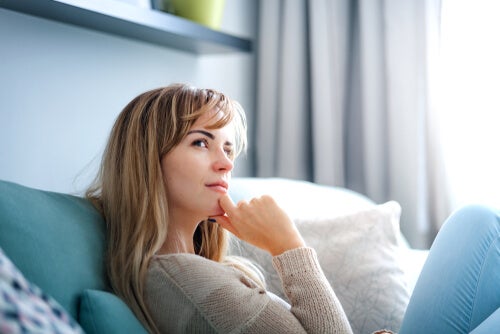 A woman sitting on the couch thinking, with her hand on her chin.