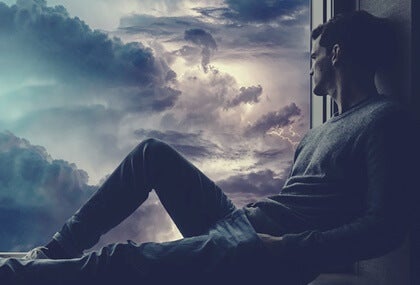 A guy looking out the window at a stormy sky.