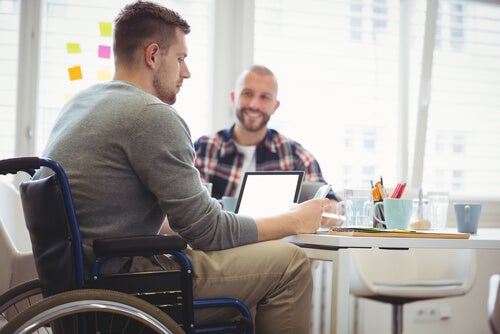 A man in a wheelchair sitting at a table working on his laptop. 