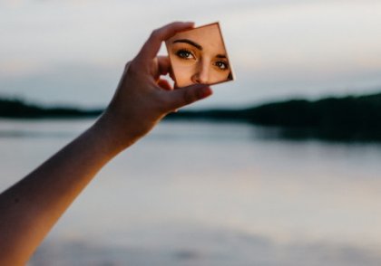 A woman looking at herself in a small square mirror.