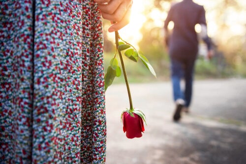 A man walking away from a woman holding a rose.