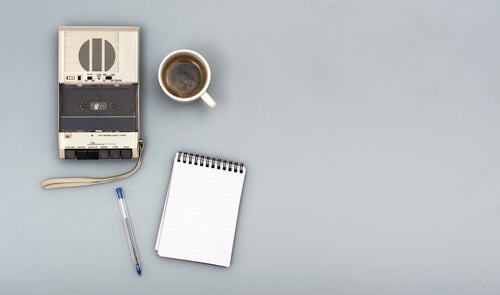 A recorder next to a cup of coffee, a pad, and a pen.
