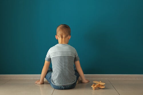 A child sitting in front of a wall with a toy plane.