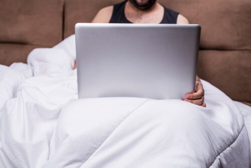 A man suffering from porn addiction using his computer in bed.
