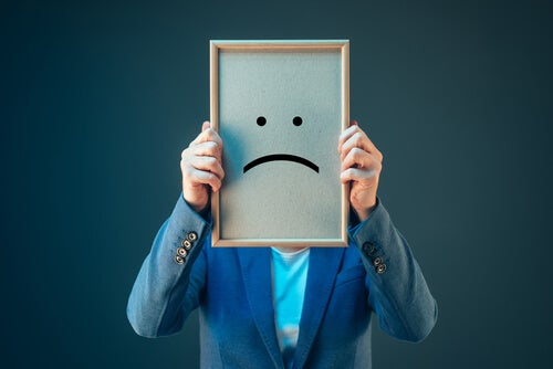 A man with a frown face on a whiteboard in front of his face.