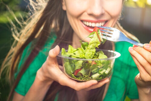 A woman smiling while pretending to eat a salad.