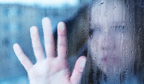 A woman with her hand on a rainy window.