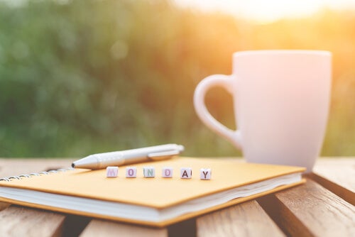 A coffee mug next to a book with the word "Monday" in block letters on it.