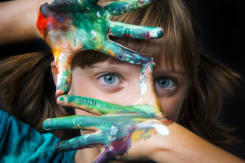 A little girl with painted hands framing her eye.