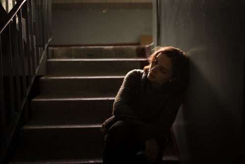A sad woman leaning against the wall on a stairwell.