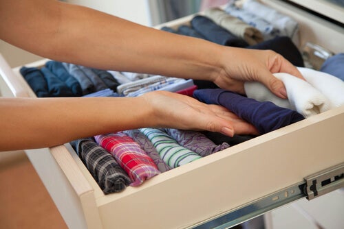 A woman organizing her folded shirts in a drawer.