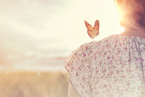 A woman standing in front of a setting sun with a butterfly on her shoulder.