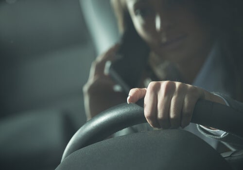A woman driving while on her phone, at risk of getting in a car crash.