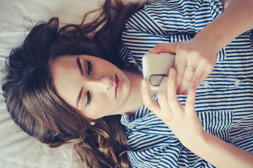 A woman lying on her bed looking at her cell phone.