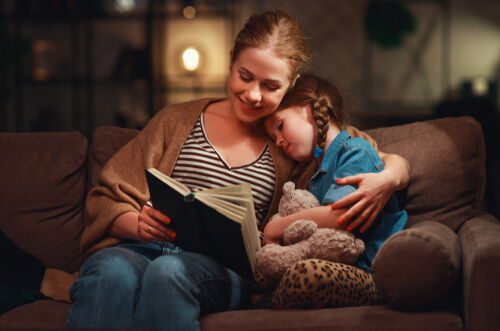 A mom on the couch reading with her daughter.