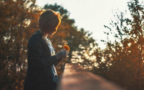 A woman outside holding a flower feeling alone.