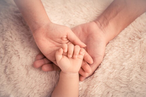 The hand of a baby on top of the hands of an adult.
