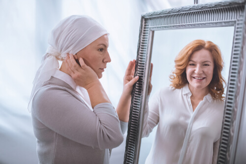 A woman with breast cancer looking at herself with hair in the mirror.