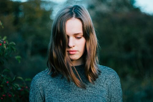 A woman with hair over her face, thinking about the nuances of atheism.