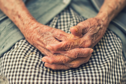 An older person's hands clasped in their lap.