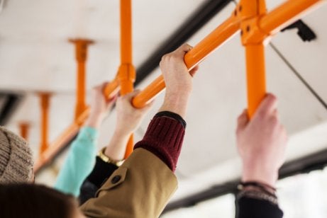 Some people holding on to the rail on a bus.
