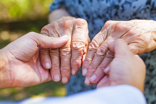 A young person holding the hands of an elderly person.