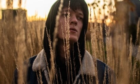 A guy walking in a field of wheat.