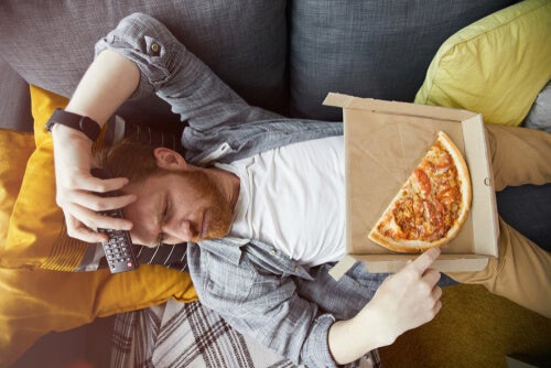 A bored man eating pizza on the couch.