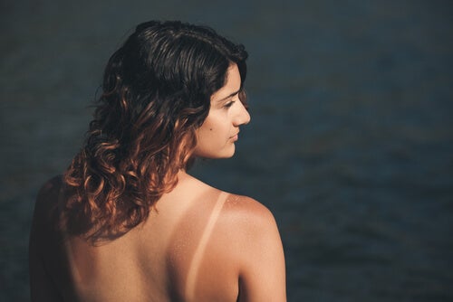 A tan woman standing in front of water.
