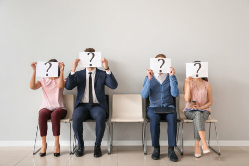 A group of people holding a sign with a question mark in front of their faces.
