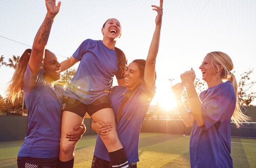 Female soccer players lifting a teammate up in the air and celebrating. 