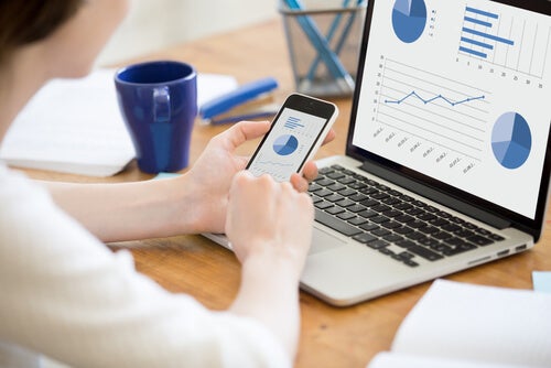 A person looking at statistics on both a phone and a computer.