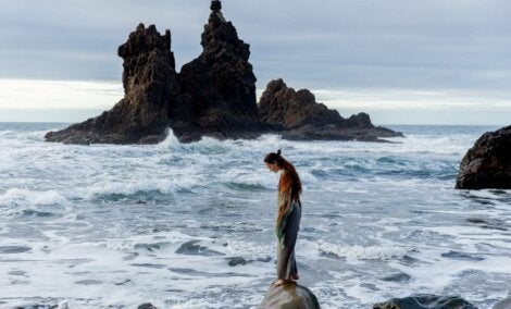 A woman standing on a rock in the ocean.