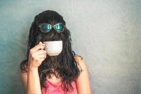A woman with hair over her face drinking coffee.