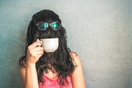 A woman with hair over her face drinking coffee.