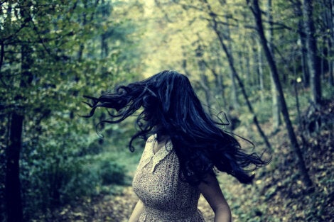 A long-haired woman running through the forest.
