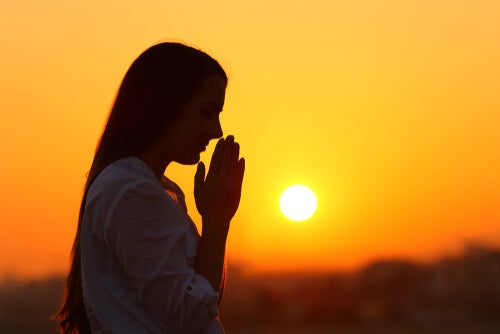 A woman's silhouette praying at dusk.