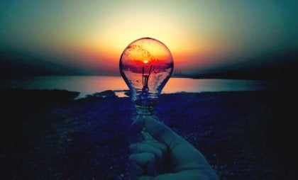 A hand holding a lightbulb in front of a sunset.