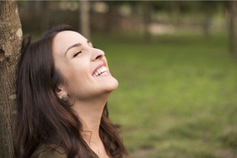 A happy woman leaning on a tree.