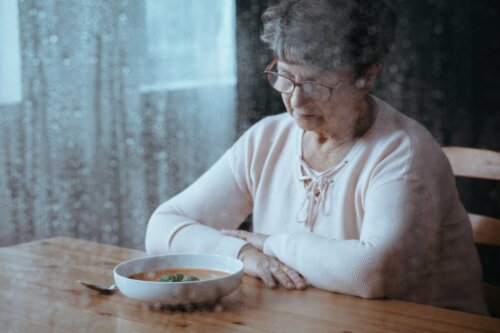 An elderly woman feeling sad looking at a plate of food.