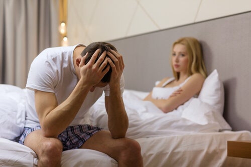 A man with post-coital depression sitting on the side of a bed and a woman in bed.
