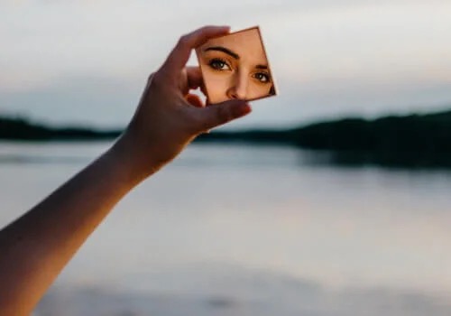 Kvinde ved sø ser sig selv i lille spejl
